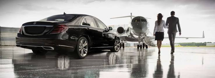 Couple walking across the tarmac toward a private jet beside a black sedan