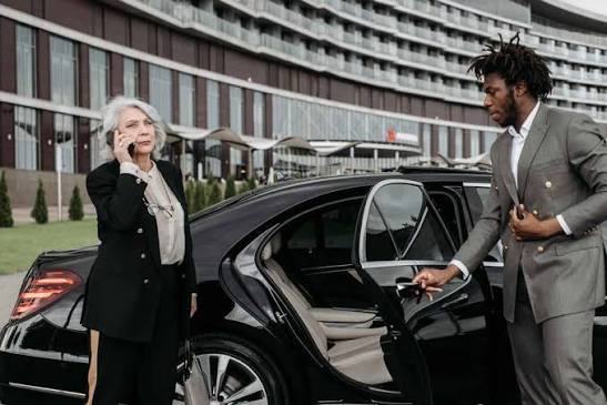 Chauffeur holding the door for a passenger beside a black sedan
